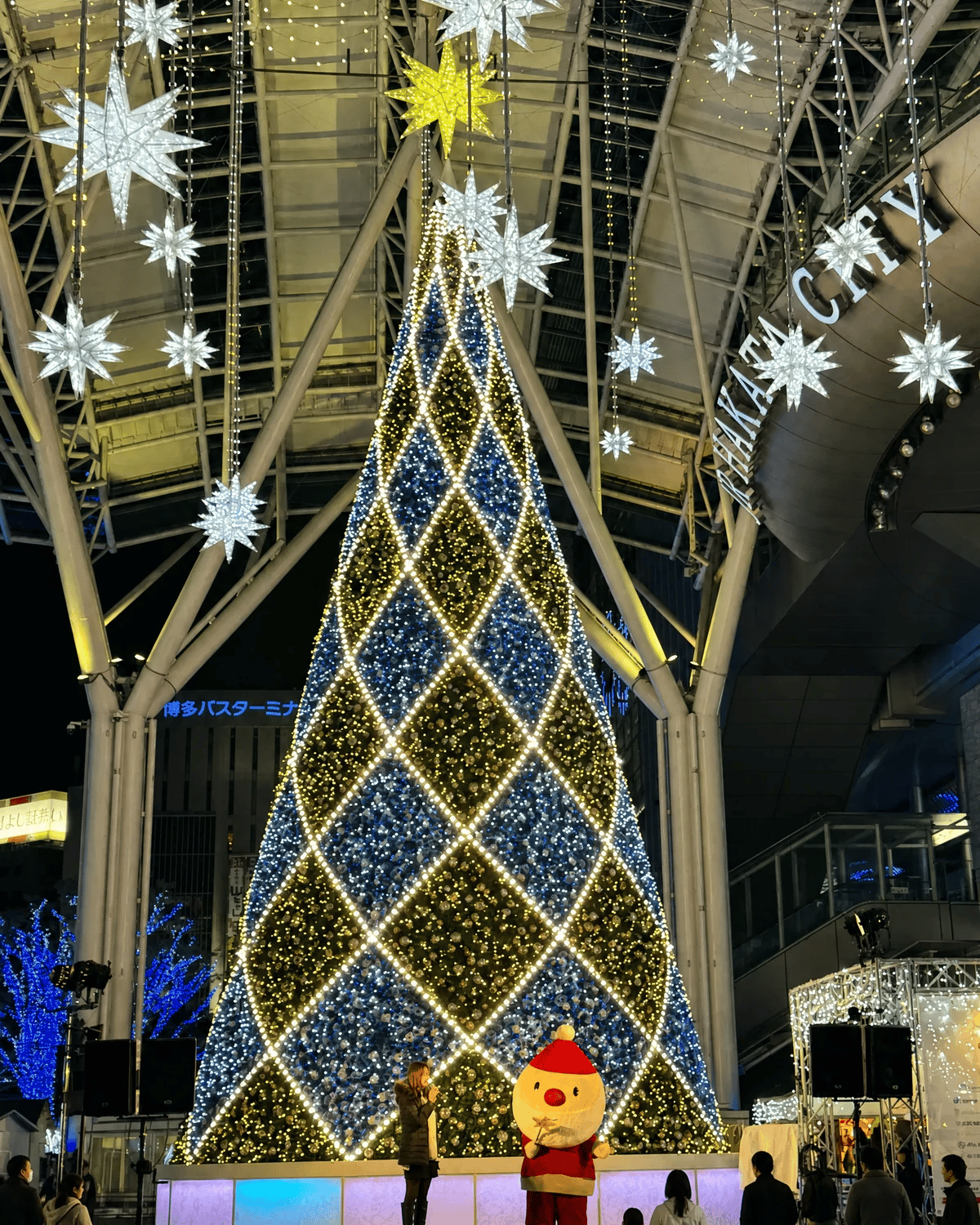 Giant illuminated Christmas tree with blue and gold LED lights during the Hikari no Machi winter light festival at JR Hakata City Station plaza in Fukuoka, Kyushu, Japan.